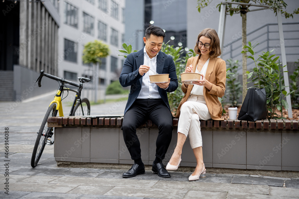 Asian businessman and caucasian businesswoman eating food and talking while having lunch at work. Co