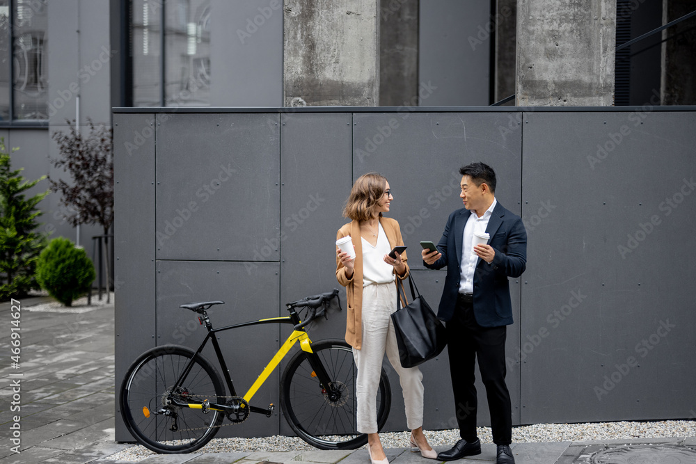 Asian businessman and caucasian businesswoman drinking coffee and using smartphones on city street w