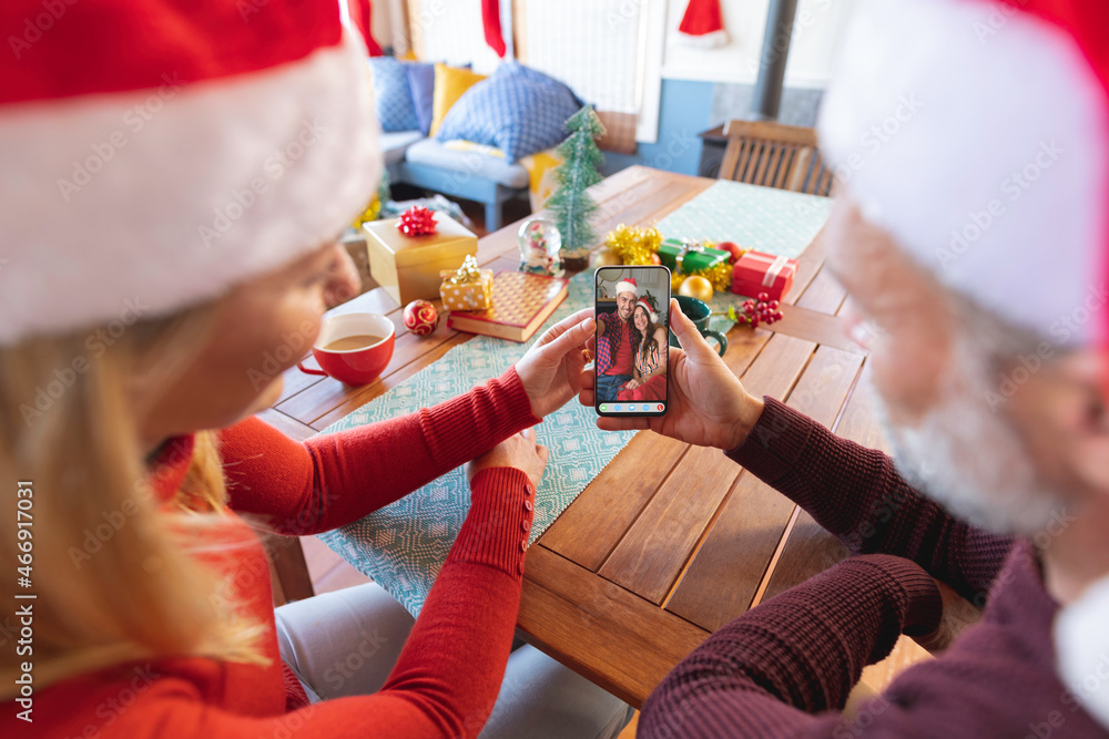 Caucasian couple in santa hats making christmas smartphone video call with smiling couple