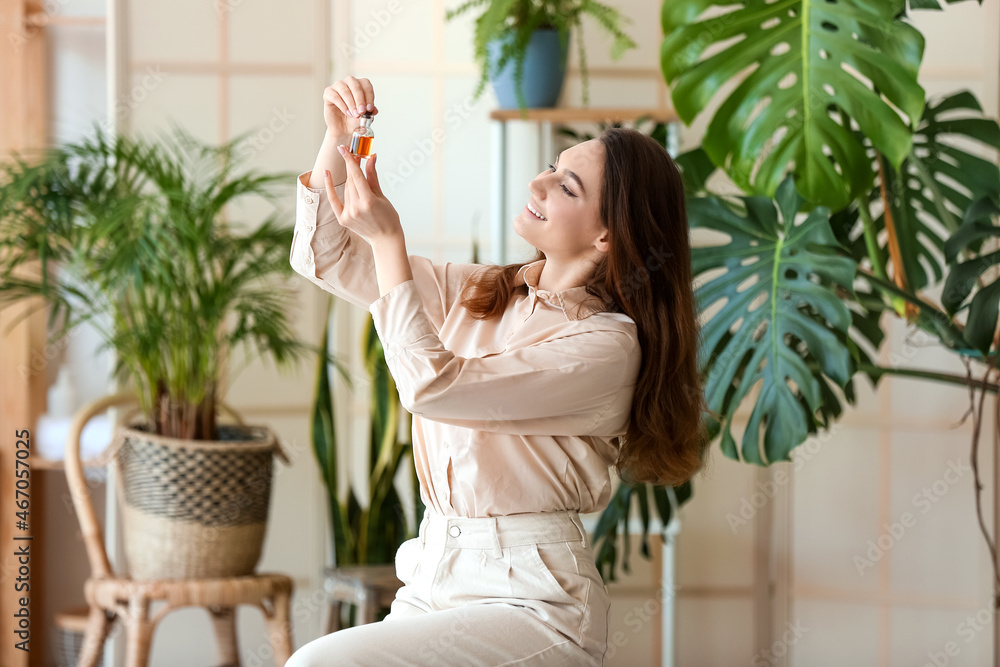 Fashionable smiling woman opening bottle of essential oil in room