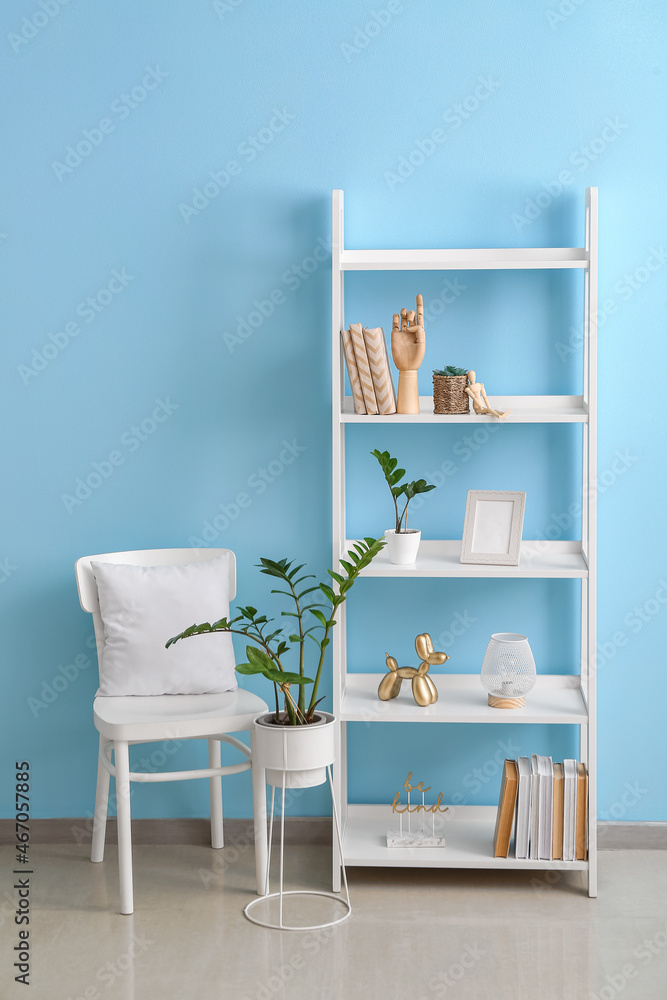 Wooden hand, books, decor on shelf unit and chair near color wall