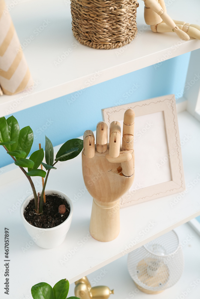 Wooden hand and houseplant on shelf near color wall, closeup