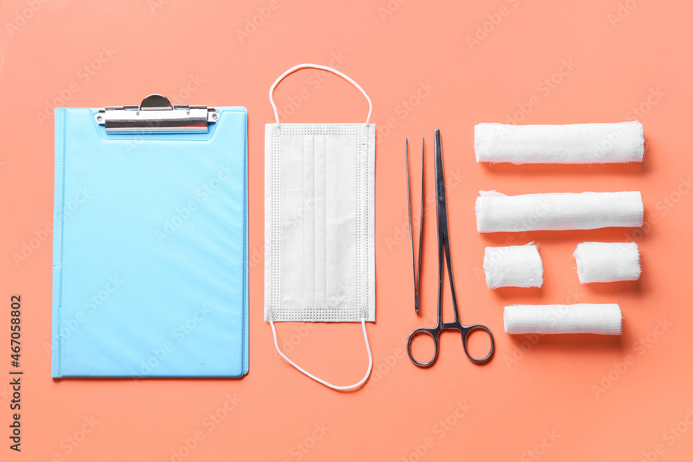 Clipboard, medical mask, surgical tools and bandage rolls on color background