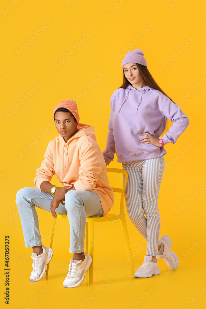 Stylish young couple in hoodies on yellow background