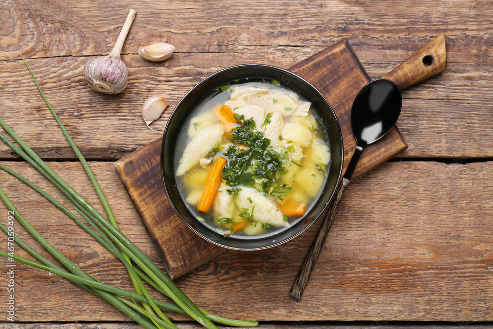 Composition with bowl of delicious dumpling soup, green onion and garlic on wooden background