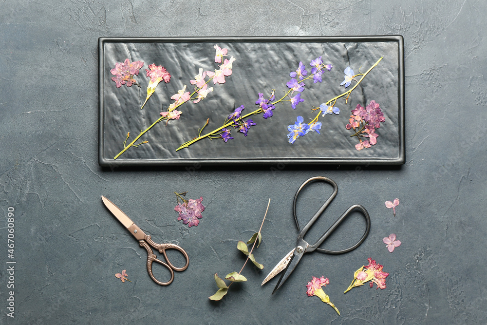 Board with dried pressed flowers and scissors on black background