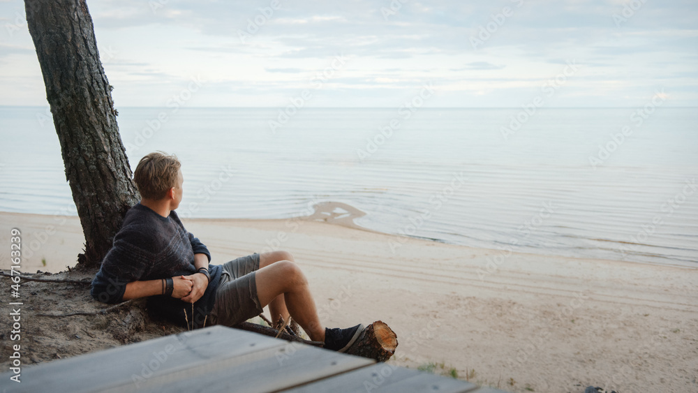 年轻英俊的男人坐在海边森林的悬崖边上。他看着大海