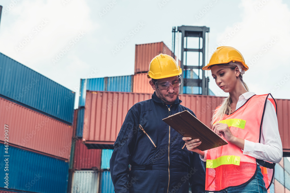 Industrial worker works with co-worker at overseas shipping container yard . Logistics supply chain 