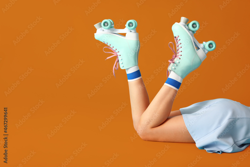 Legs of young woman in roller skates on orange background