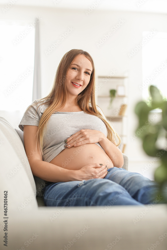 Young pregnant woman sitting on grey sofa at home