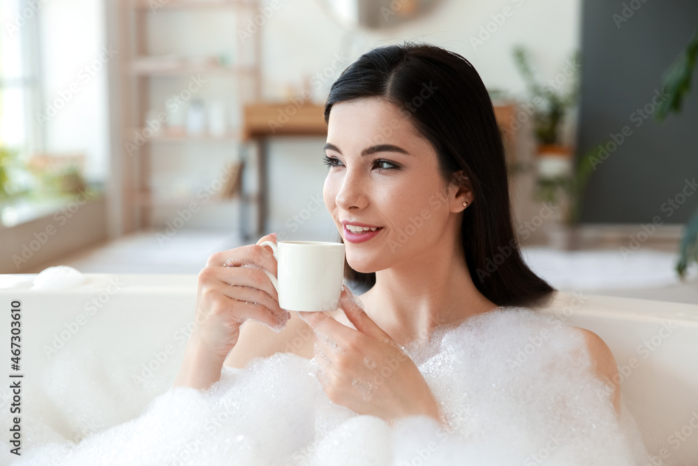 Relaxed young woman with cup of coffee taking bath at home