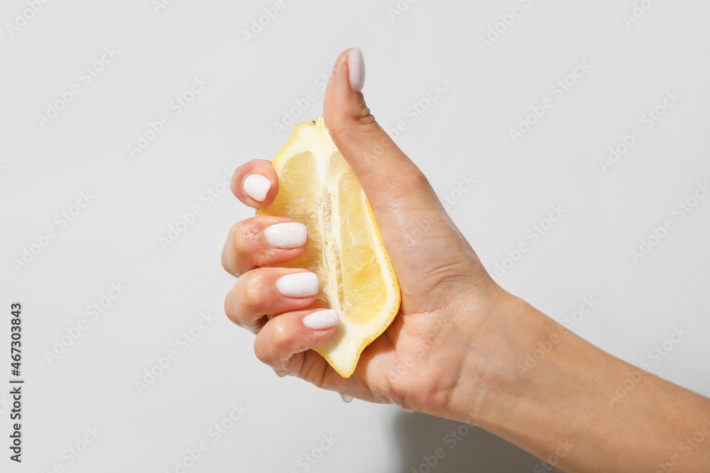 Woman with beautiful manicure squeezing sliced lemon on light background