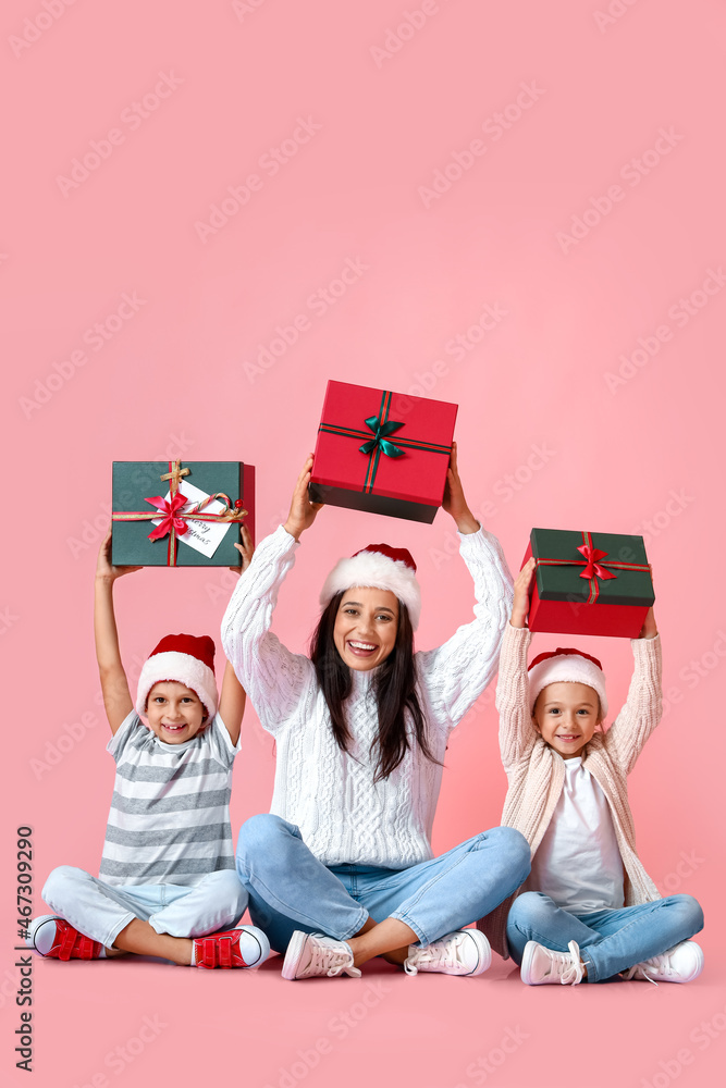 Young mother with her little kids and Christmas gifts on pink background