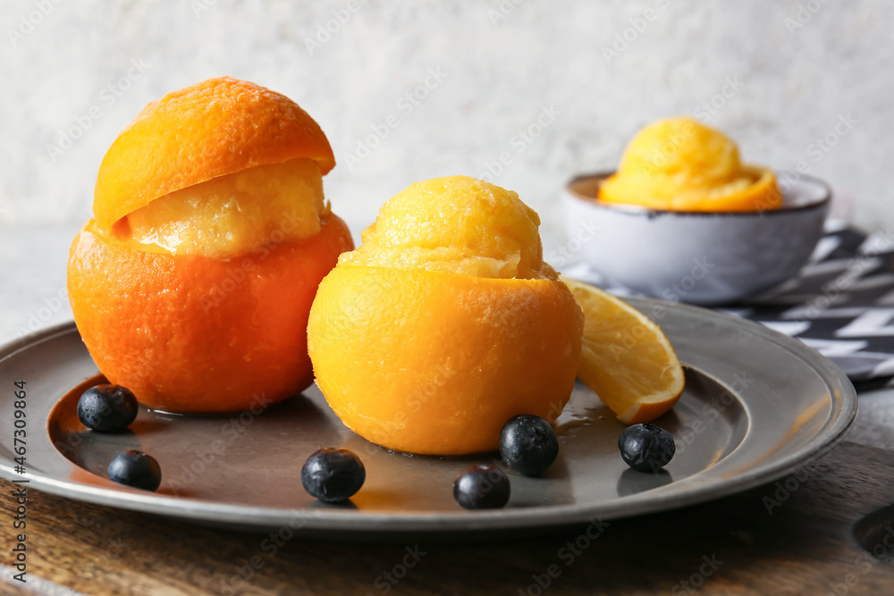 Plate with tasty ice creams in orange peels on grey background