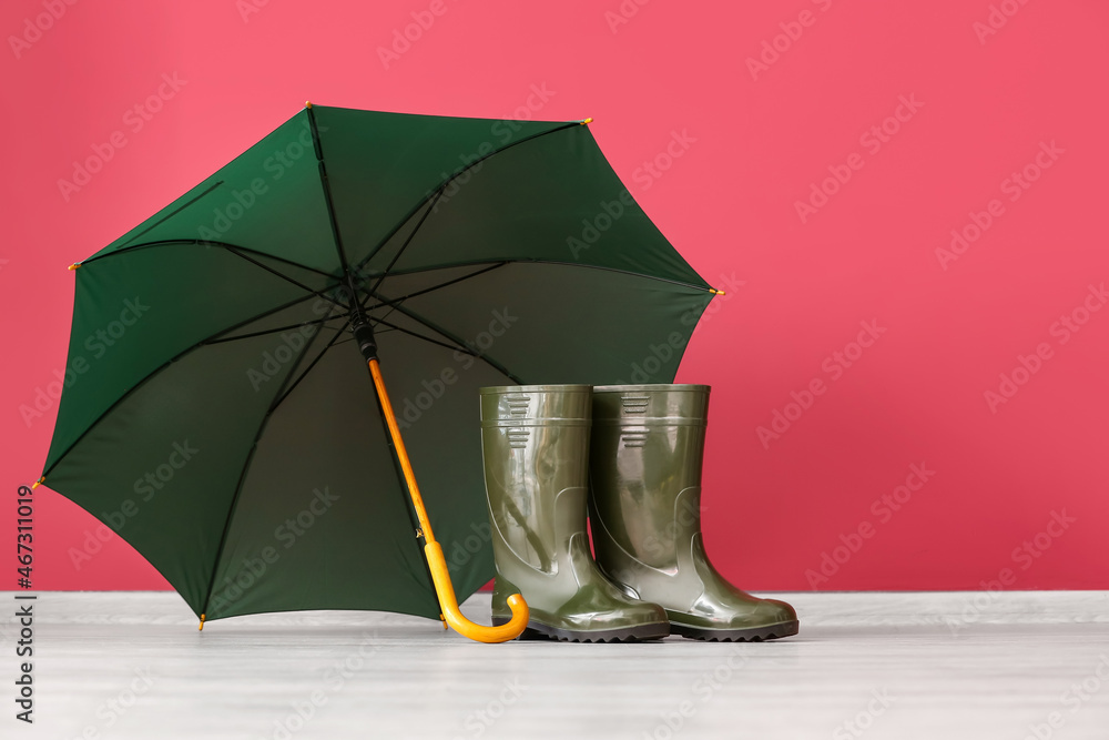 一双橡胶雨靴和雨伞放在靠近彩色墙的地板上