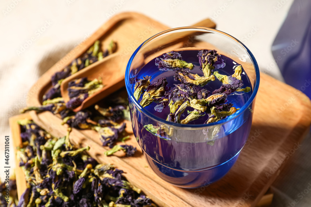 Wooden board with glass of blue tea and dried flowers on table