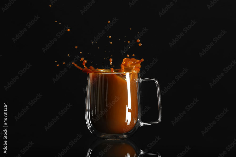 Glass cup of tasty iced coffee with splashes on black background