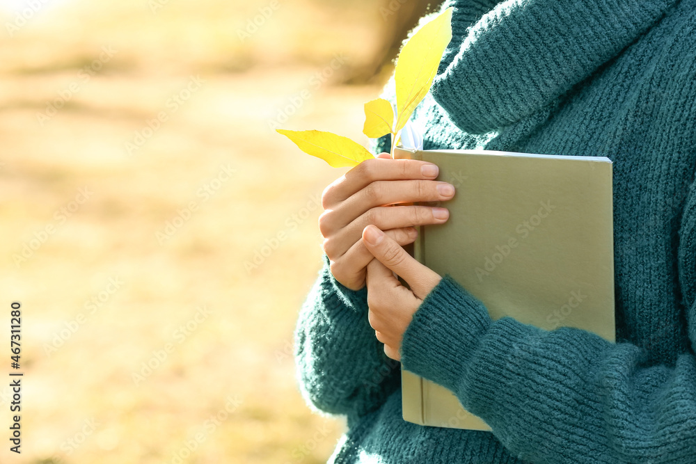 Woman with book and autumn leaf in park, closeup