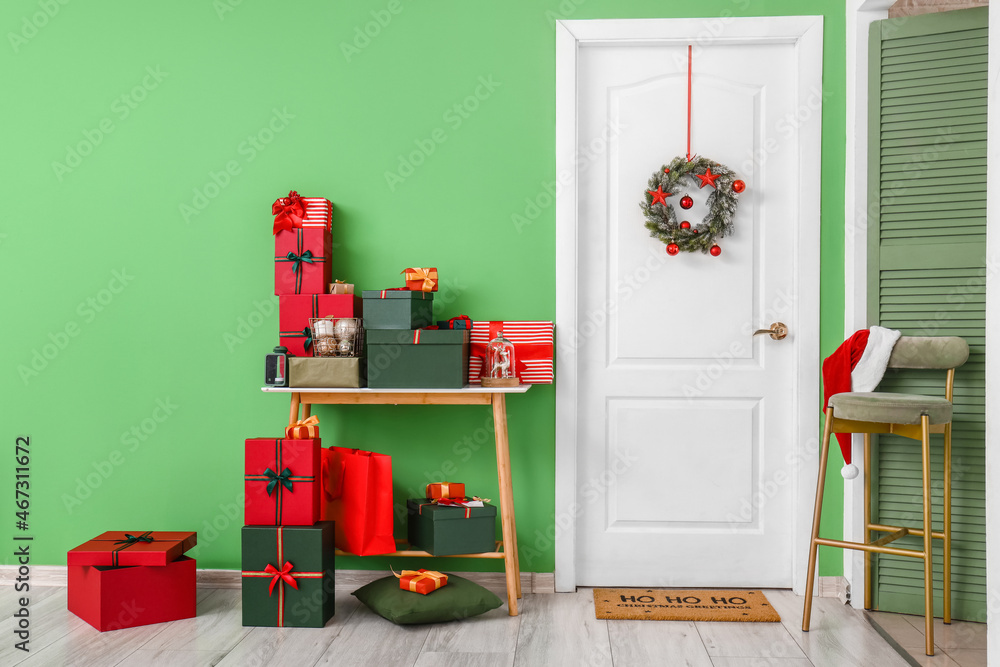 White door with wreath, table and Christmas gifts near green wall