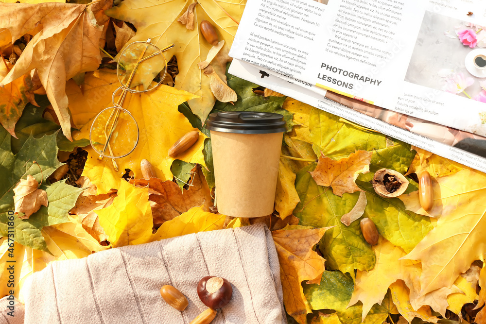 Takeaway cup of tasty coffee, newspaper and sweater on fallen leaves