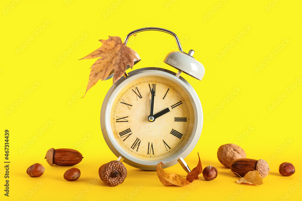 Alarm clock and autumn leaves with nuts on color background. Daylight saving time end