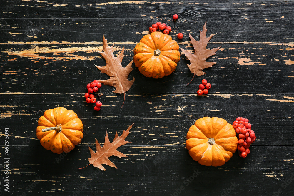 Ripe pumpkins, rowan berries and autumn leaves on dark wooden background