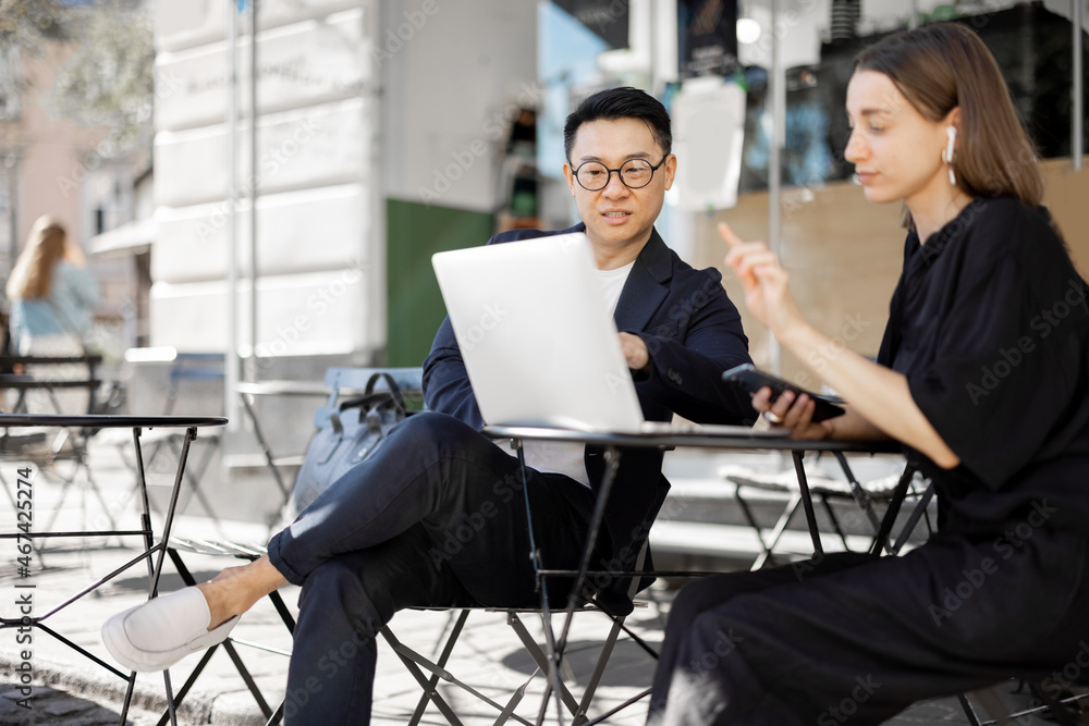 Multiracial business people watching something on laptop during work at outdoor cafe. Concept of rem