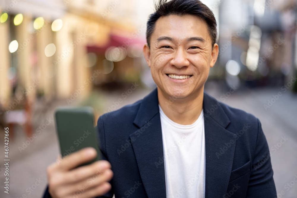 Portrait of asian man holding smartphone and looking at camera. Concept of modern successful man. Sm