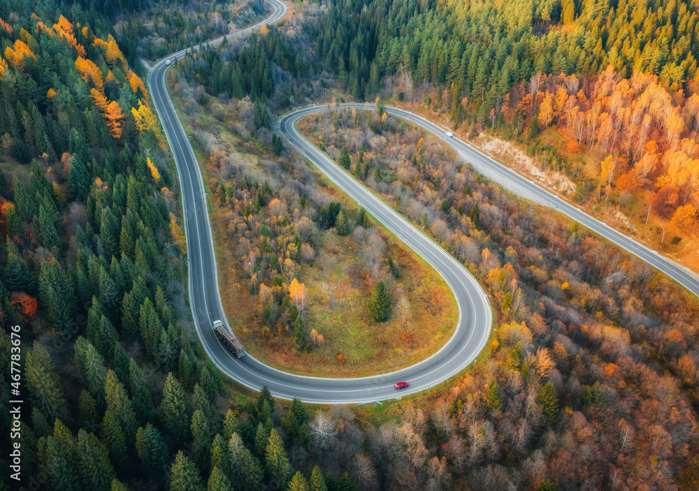 秋天日落时，彩色森林中蜿蜒的道路鸟瞰图。无人机俯瞰山脉