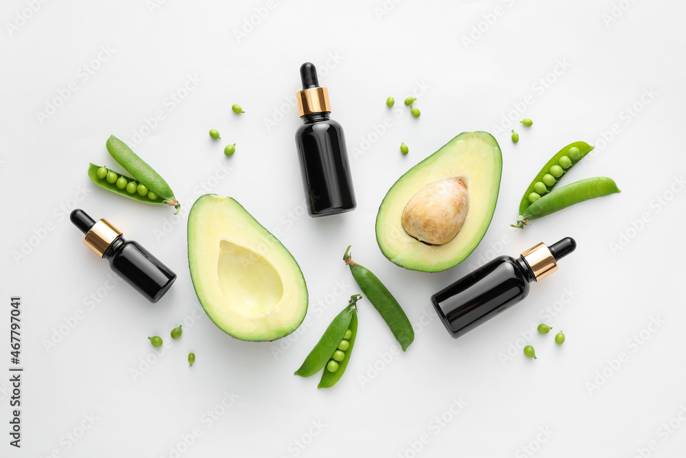 Bottles of essential oil, avocado and green peas on white background