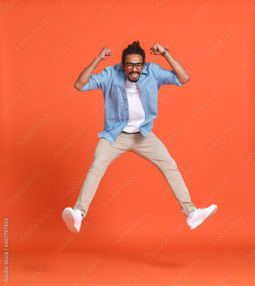 Full length shot of young emotional overjoyed african american man jumping over orange background