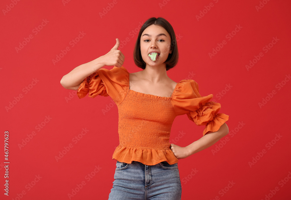 Young woman with chewing gum showing thumb-up on color background