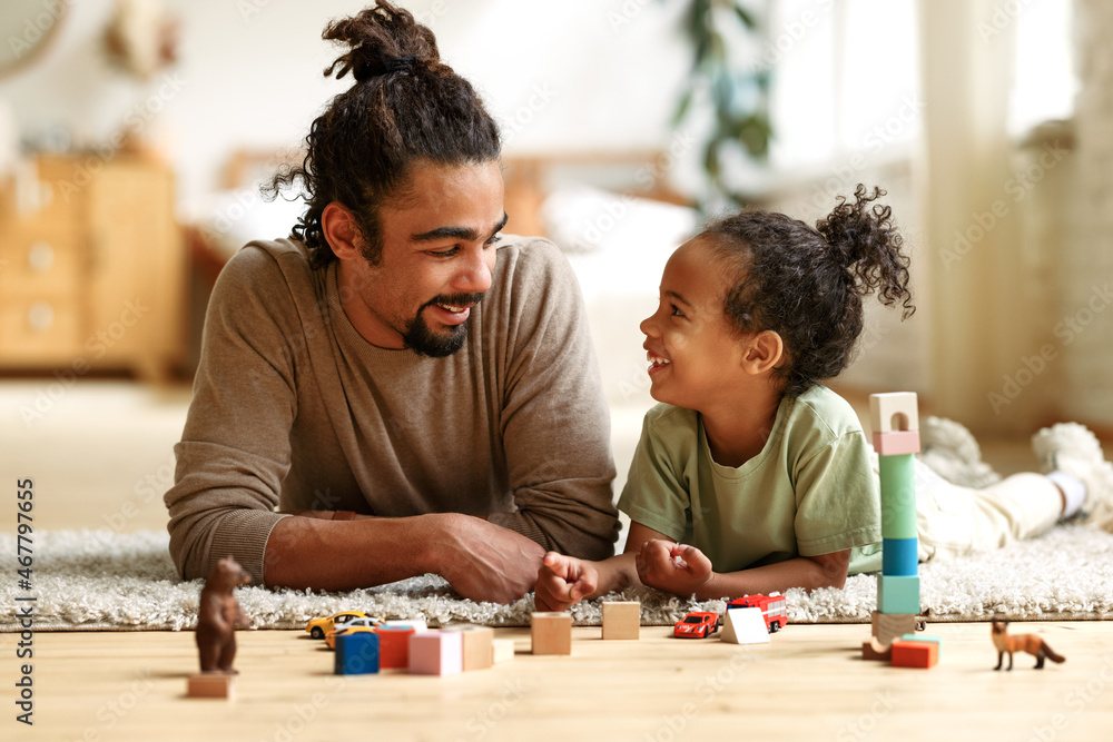 Happy african american family father and child son laughing while playing toys together at home