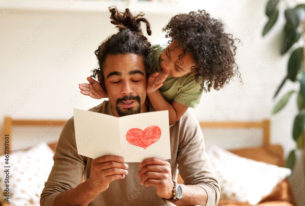 Smiling afro american boy son covering eyes of father with hands and congratulating him on holiday