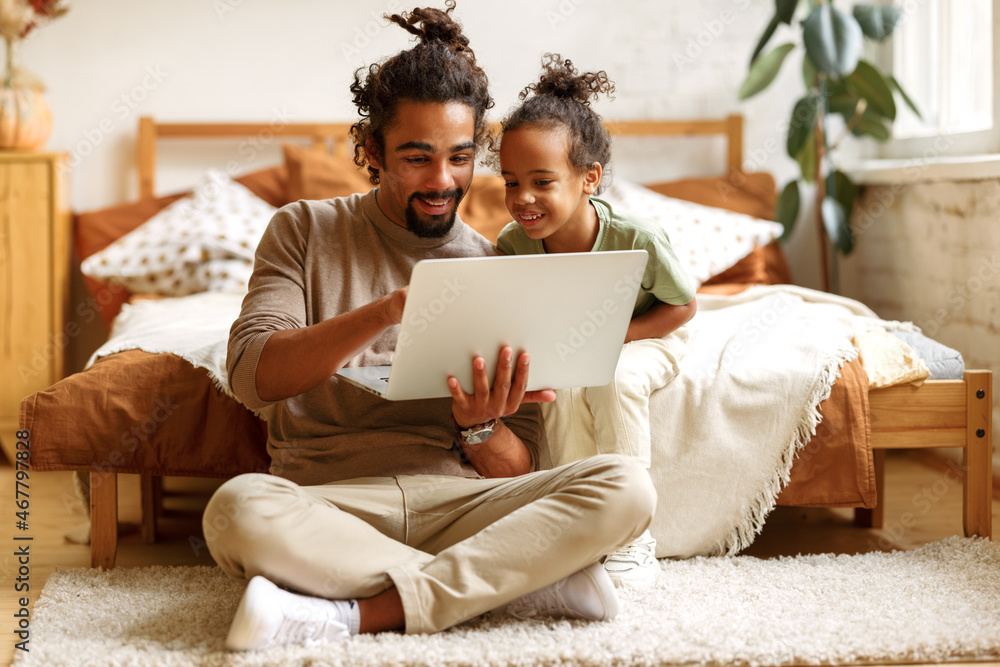 Happy african american family little son with dad watching funny videos on laptop together at home