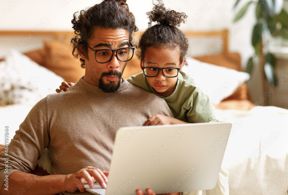 Happy african american family little son with dad watching funny videos on laptop together at home