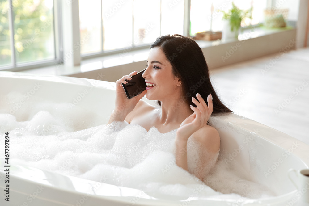 Relaxed young woman talking by mobile phone while taking bath at home