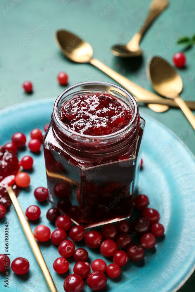 Jar of tasty cranberry jam and fresh berries on green background