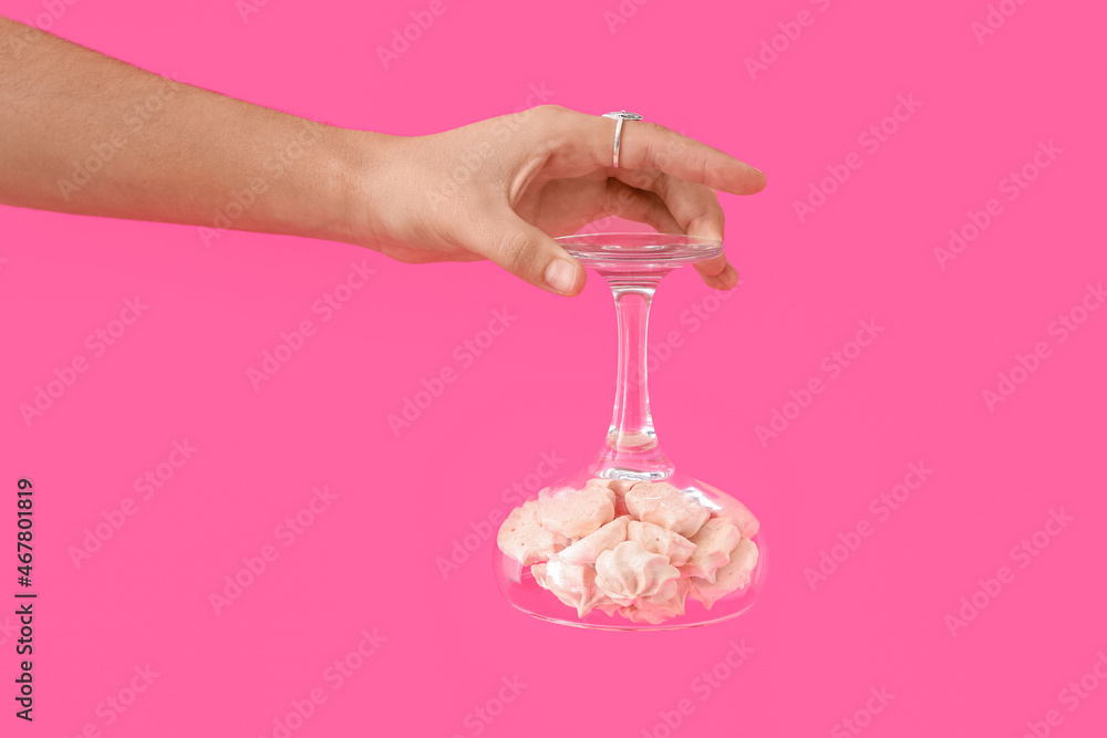 Female hand with tasty meringues in glass on color background