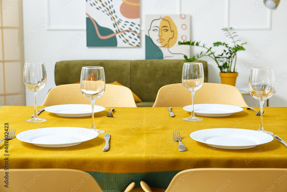 Dining table with yellow cloth, plates and glasses in room