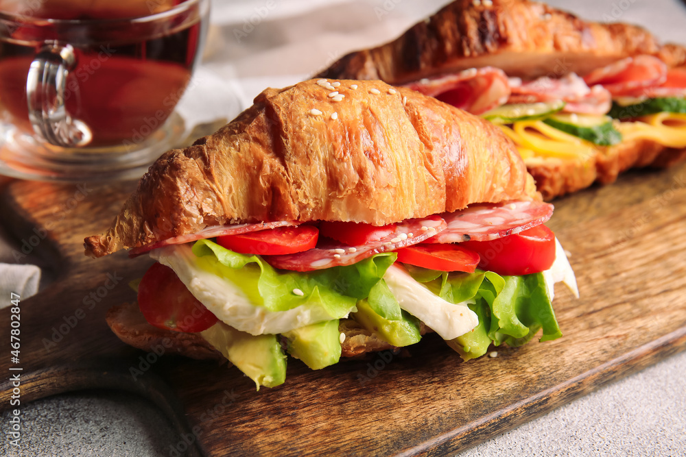 Wooden board with delicious croissant sandwiches on light background