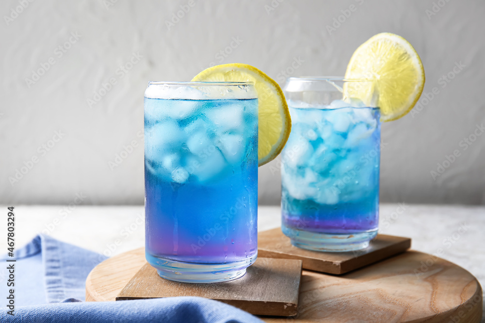 Glasses of iced blue tea and lemon on light background, closeup