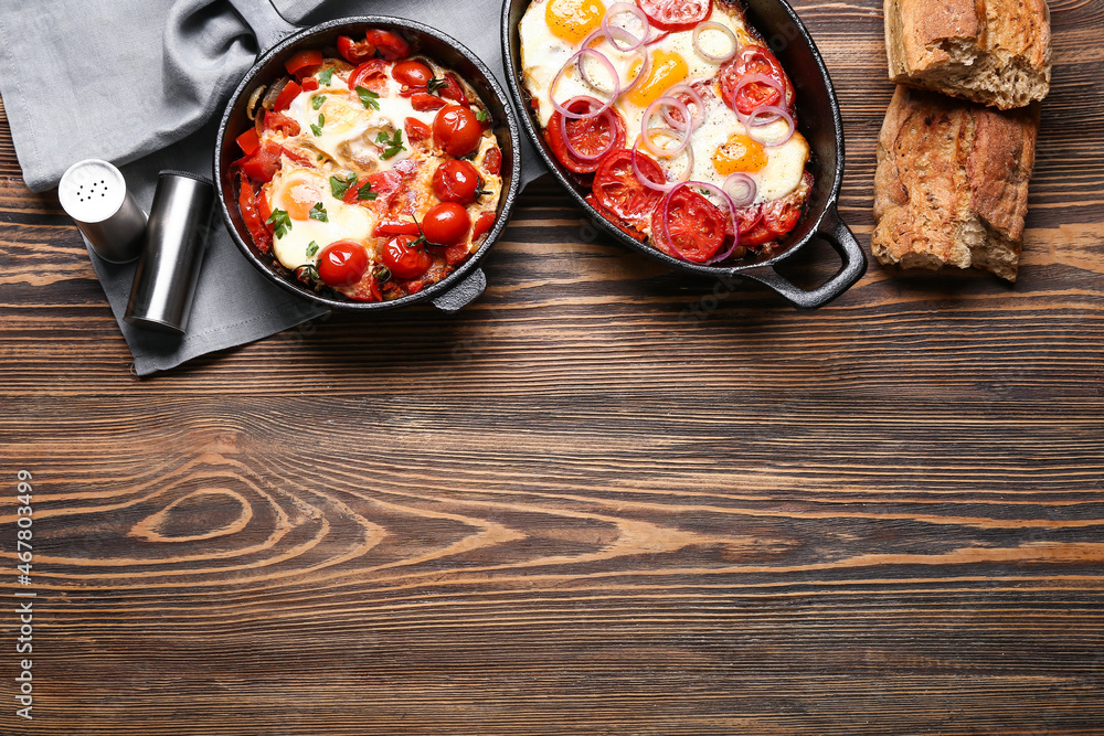 Baking dish and frying pan with tasty Shakshouka on wooden background