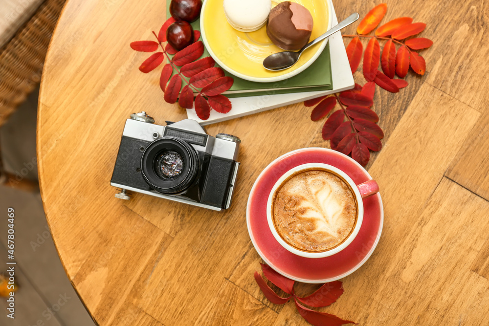 Cup of tasty coffee, photo camera and dessert on table in cafe