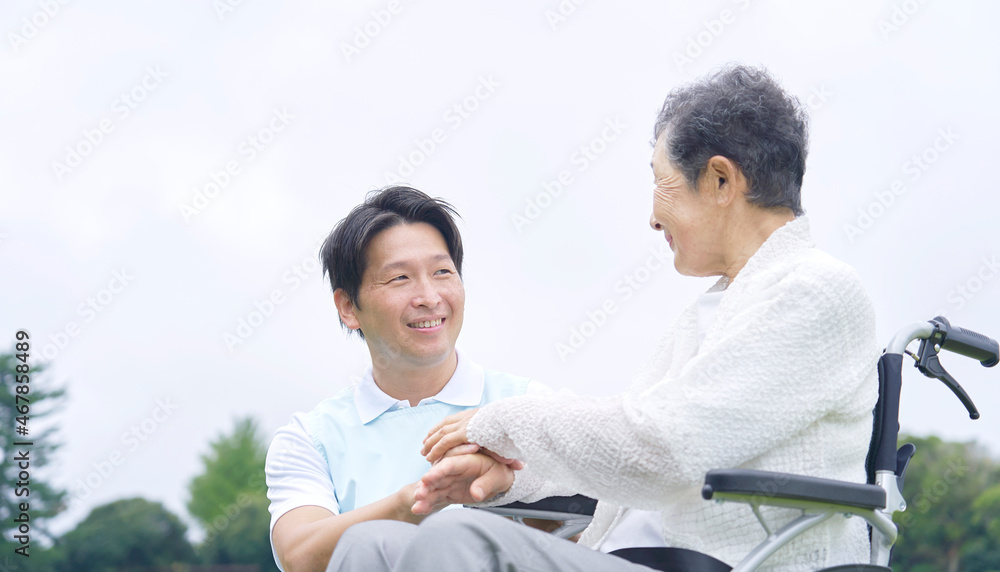 介護士と車椅子に乗る高齢者　屋外