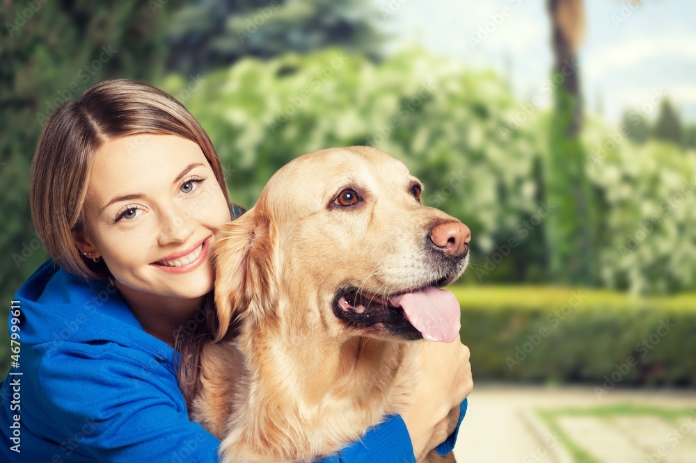 Smiling young attractive woman playing with cute puppy dog on summer outdoor background.