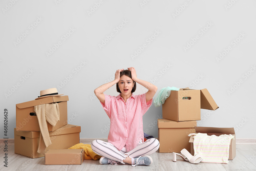 Stressed young woman with wardrobe boxes and things near light wall