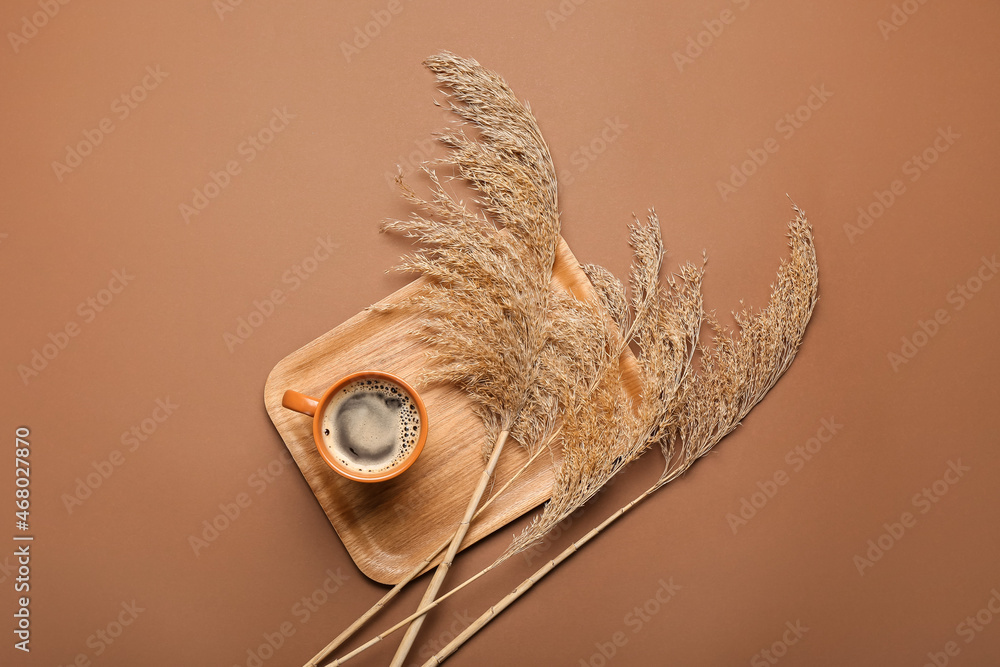 Wooden tray with cup of coffee and dry reeds on color background