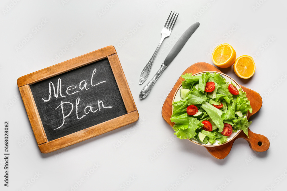 Chalkboard with words MEAL PLAN and fresh salad on white background