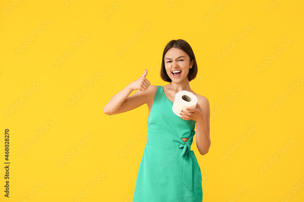 Young woman with toilet paper showing thumb-up on color background